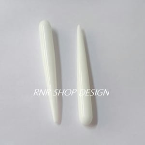 Può includere: Due strumenti in ceramica bianchi e appuntiti. Gli strumenti sono lunghi circa 10 cm e hanno una finitura liscia e lucida.