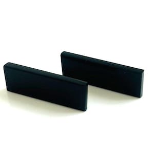 Könnte beinhalten: Zwei schwarze rechteckige Blöcke, möglicherweise aus Holz oder Kunststoff, werden auf einer weißen Oberfläche gezeigt. Die Blöcke sind glatt und haben eine matte Oberfläche.