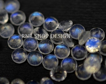 May include: A collection of iridescent white moonstone beads with a blue sheen. The beads are round and have a faceted surface. RNR SHOP DESIGN is printed on the image.