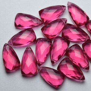 May include: A selection of faceted, teardrop-shaped gemstones in a vibrant magenta hue. The gems are arranged on a white surface, showcasing their polished surfaces and internal facets. The gemstones are ideal for jewelry making.