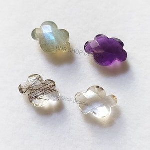 May include: Four gemstone flower-shaped cabochons. One is clear, one is light grey with iridescent shimmer, one is amethyst purple, and one is clear with brown inclusions.
