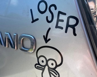 May include: A black vinyl sticker on a silver car. The sticker features the word "LOSER" above a cartoon drawing of Squidward Tentacles from Spongebob Squarepants, with an arrow pointing to the character.