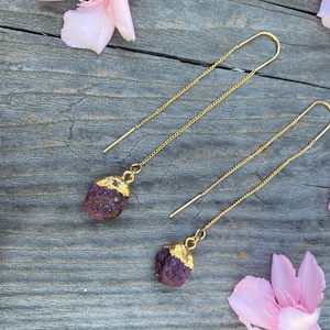 Puede incluir: Un par de pendientes de cadena dorada con una piedra preciosa púrpura y dorada que cuelga al final de cada cadena.