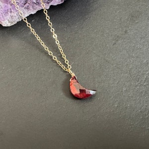 Pode incluir: Um colar de corrente de ouro com um pingente de lua crescente feito de granada vermelha.