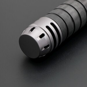 May include: Close-up of a metallic gray cylindrical object with a textured grip and a rounded end. The object has a series of vertical slots and circular openings near the end, and a diamond pattern on the grip.