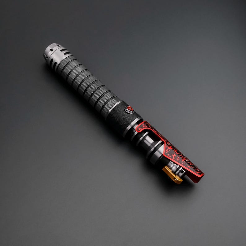 May include: A metallic lightsaber with a black grip and red accents. The hilt features a textured design and a red button. The blade emitter is red with intricate patterns and a gold-colored detail.