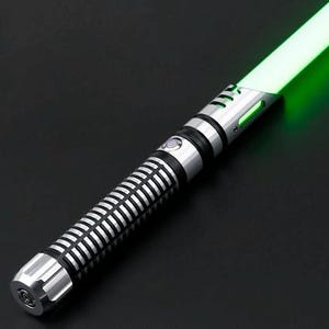 Pu&ograve; includere: Una spada laser argento e nera con una lama verde brillante. L'elsa presenta un design a coste e un pulsante circolare. La lama emette un bagliore verde vibrante su uno sfondo nero.