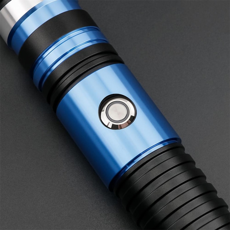 May include: A close-up of a blue and black lightsaber hilt. The hilt features a metallic blue finish with black bands and a silver button. The design is sleek and modern, with a focus on the details of the hilt.