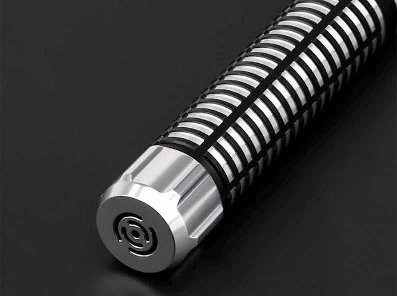 Pu&ograve; includere: Primo piano di un oggetto cilindrico con base in metallo argentato e corpo a motivi neri e argentati. L'estremit&agrave; dell'oggetto presenta un disegno circolare. L'oggetto &egrave; su una superficie nera.