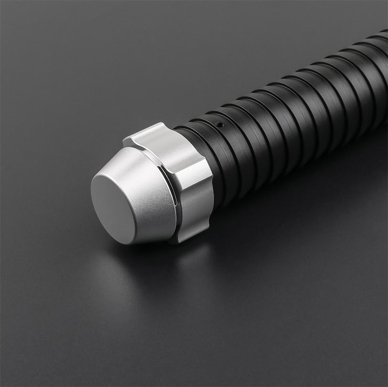 May include: Close-up of a black and silver lightsaber hilt. The hilt features a ribbed black grip and a silver pommel and emitter. The lightsaber is set against a dark background.