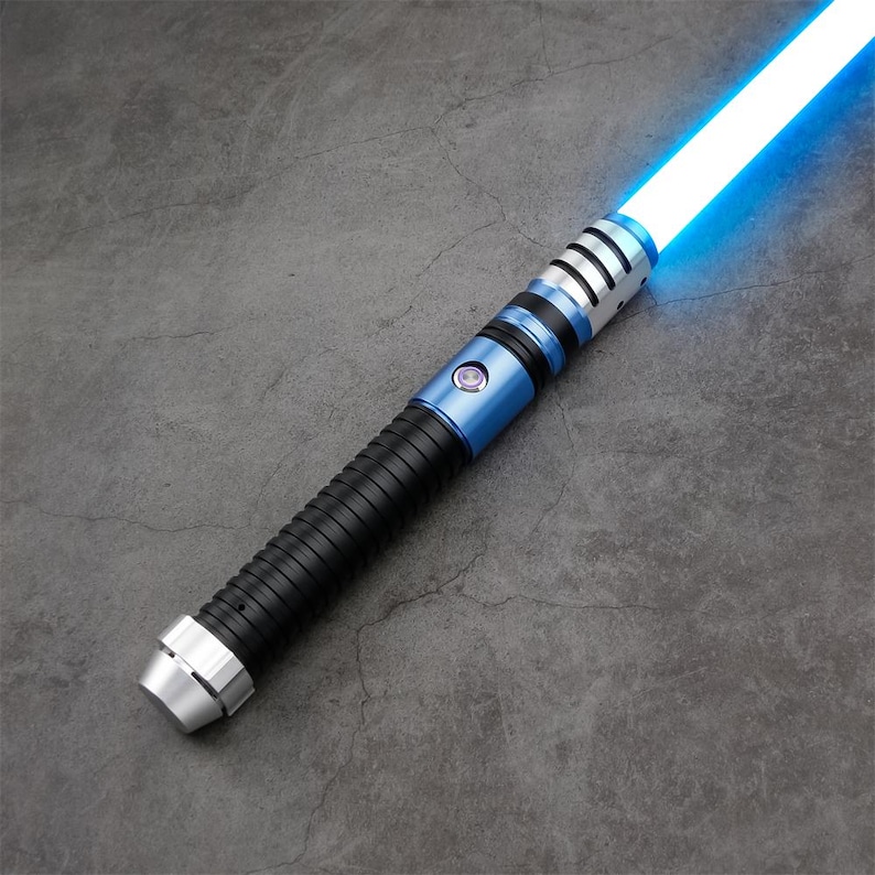 May include: A blue and silver lightsaber with a bright blue blade. The hilt features a black ribbed grip, a blue section with a button, and silver accents. The blade emits a bright, glowing blue light.