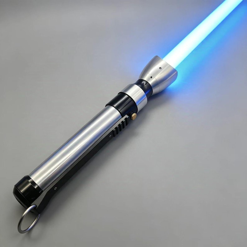 May include: A silver and black lightsaber with a bright blue blade. The hilt features a metallic finish with black accents and a ring at the base. The glowing blade emits a vibrant blue light.