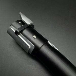 May include: A black and silver lightsaber hilt. The hilt has a cylindrical black grip with silver accents near the emitter and a silver blade guard. The design is sleek and modern, with a focus on metallic finishes.