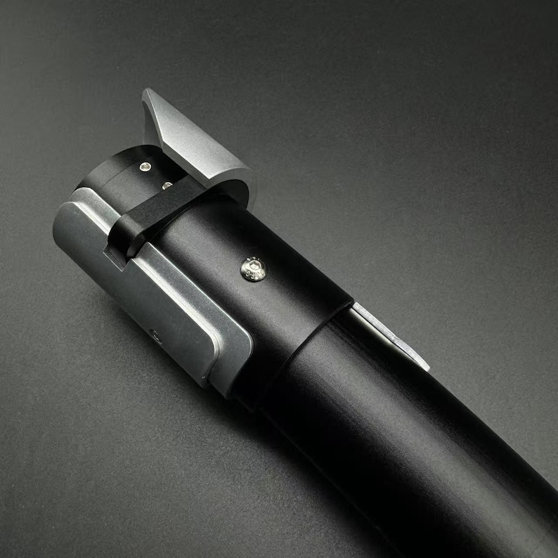May include: A black and silver lightsaber hilt. The hilt has a cylindrical black grip with silver accents near the emitter and a silver blade guard. The design is sleek and modern, with a focus on metallic finishes.