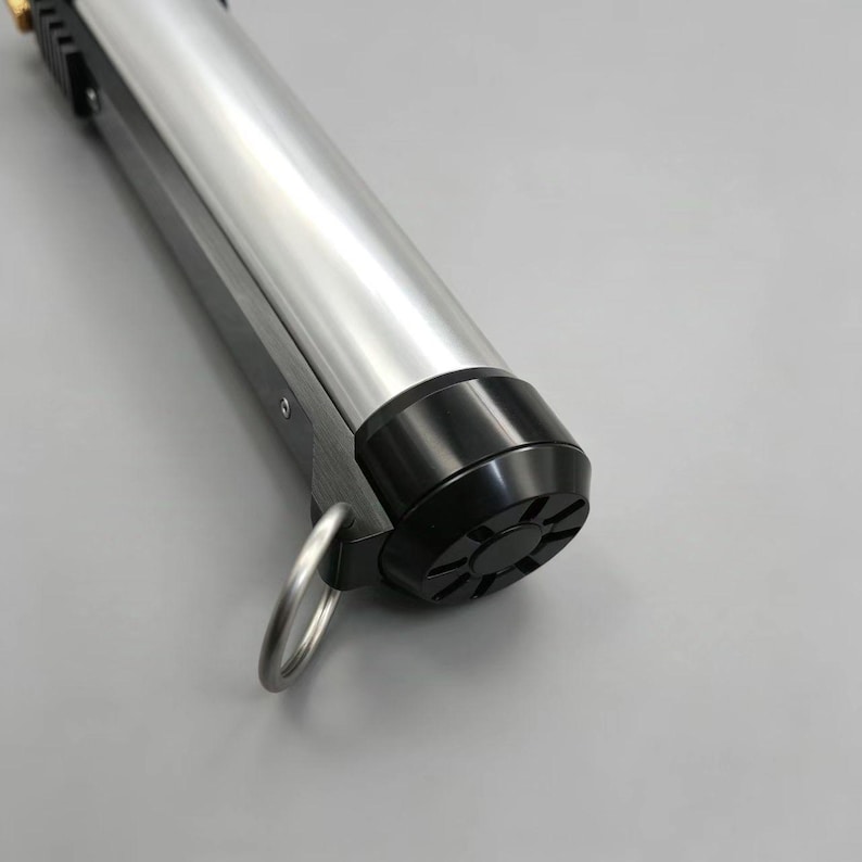 May include: A silver and black cylindrical object with a ring attached. The object has a metallic silver body and a black base with a starburst pattern. The object is likely a tool or a part of a larger device.