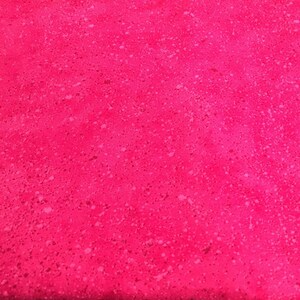 May include: A close-up of a bright pink fabric with a speckled pattern. The fabric is folded and placed on a ruler.