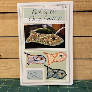 May include: A pattern titled "Fish in the Oven (mitt)!" featuring a fish-shaped oven mitt design. The image shows a finished mitt and three additional fish-shaped designs in various colors and patterns. The Vanilla House Designs logo is also visible.