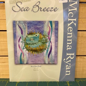 May include: A package for a quilting project titled "Sea Breeze" by McKenna Ryan. The package features a colorful illustration of a pufferfish, with the text "Koo Koo Puff" and dimensions of 12" x 12".