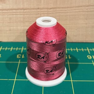 May include: A spool of pink embroidery thread with the brand name "RA" printed on the side.