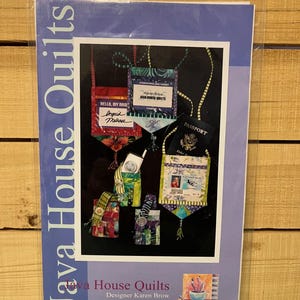 May include: A package featuring a colorful quilt pattern by Java House Quilts. The pattern showcases various small fabric pouches with text that reads "Hello, My Name" and "Passport". The package is sealed in clear plastic.
