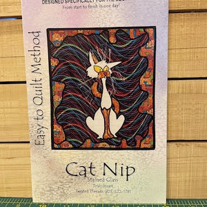 May include: A sewing pattern titled "Cat Nip" with a stained glass cat illustration. The cover reads "Designed Specifically for the Beginner!" and "Easy to Quilt Method." The cat design features white, orange, and black colors with a colorful background.