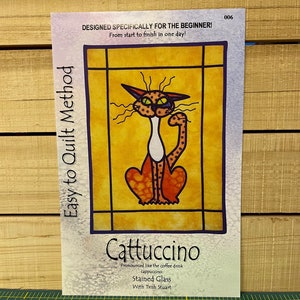 May include: A stained glass pattern of a cat with orange and white fur, sitting on a yellow background. The pattern is titled "Cattuccino" and is described as "Pronounced like the coffee drink cappuccino" and "Stained Glass with Trish Stuart".