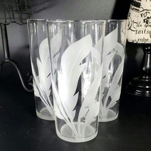 May include: Four clear glass tumblers with a frosted feather design. The tall glasses are ideal for serving drinks. The feather design adds a touch of elegance. Each glass is approximately 15 cm tall, suitable for water, juice, or cocktails.