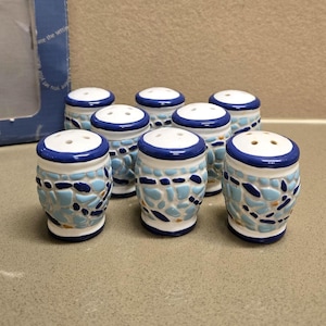 May include: Eight ceramic salt and pepper shakers with blue and white mosaic designs. The shakers are all the same size and shape, and they have a small hole in the top for pouring.