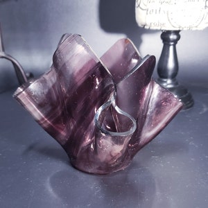 May include: A purple glass vase with a unique, wavy design. The vase is made of clear glass with a purple swirl pattern.
