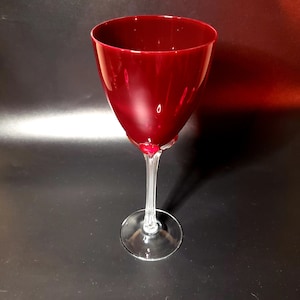May include: A tall, clear wine glass with a deep red bowl. The glass has a long, thin stem and a round base.