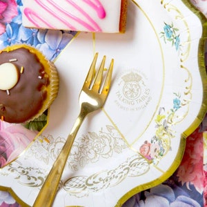 May include: A white paper party plate with a gold scalloped edge and floral design. The plate features a gold logo that says "Talking Tables, Brewed in England".