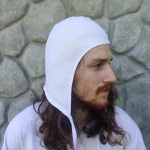 May include: A white linen coif with a long pointed flap in the back. The coif is worn by a person with long brown hair.
