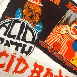 Puede incluir: Varios parches de tela con las palabras "ACID BATH" en naranja, con letras estilizadas. Un parche presenta una calavera con un sombrero rojo. Otro muestra un payaso con el texto "When the kite string pops".