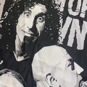 Pode incluir: Gr&aacute;fico a preto e branco com dois retratos estilizados. Um retrato retrata um homem com cabelo encaracolado, o outro um homem careca. A palavra "SYSTEM" &eacute; vis&iacute;vel na parte superior da imagem, e a palavra "OF" &eacute; vis&iacute;vel &agrave; direita.