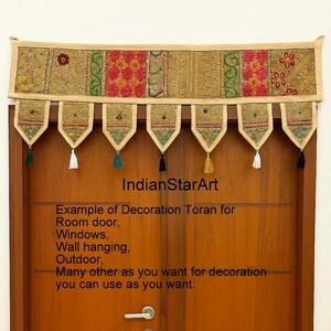Puede incluir: Un toran textil decorativo, con un panel superior beige con patrones florales y geométricos bordados en rojo, verde y dorado. Debajo, siete elementos en forma de colgante con borlas cuelgan sobre una puerta de madera. Texto: IndianStarArt.