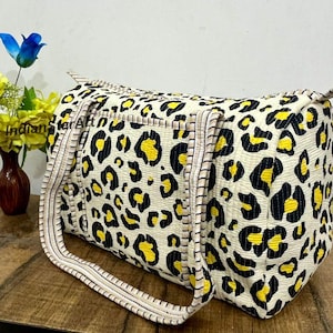 May include: A cream-colored duffel bag with a leopard print pattern in black and yellow. The bag has two handles and a zipper closure. The bag is approximately 18 inches long.