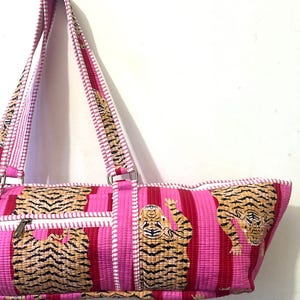 May include: Pink and red striped tote bag with a tiger print. The bag has a zipper closure and white trim. The straps are pink and white striped. The bag is made of a quilted fabric.