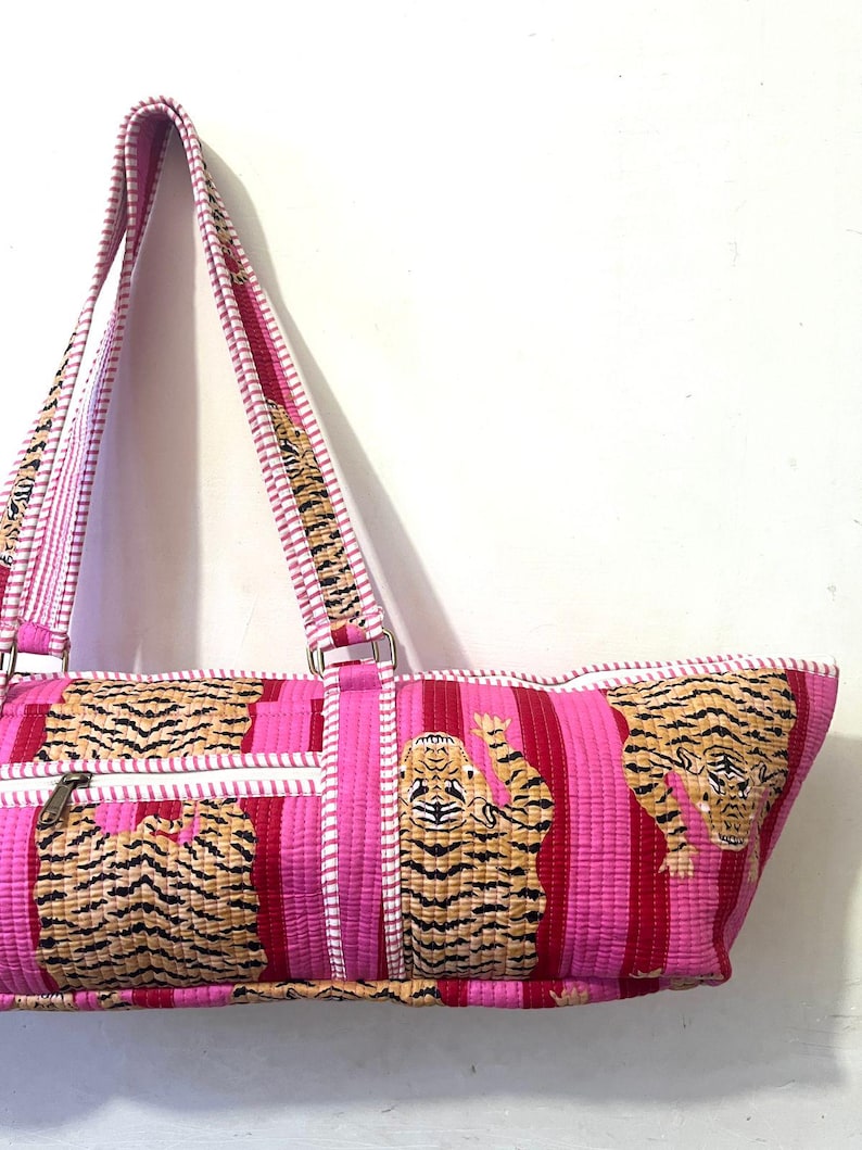 May include: Pink and red striped tote bag with a tiger print. The bag has a zipper closure and white trim. The straps are pink and white striped. The bag is made of a quilted fabric.