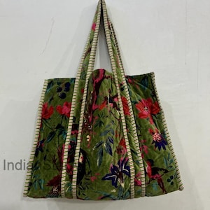 May include: A green velvet tote bag with a floral pattern in red, pink, and blue. The bag has quilted detailing and striped trim along the edges and handles. The bag is designed for carrying items.