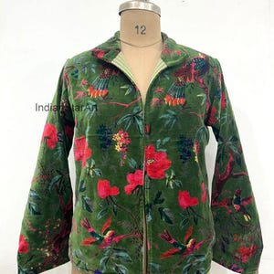 Peut inclure: Veste en velours vert avec un imprimé floral et d'oiseaux. La veste a un col et des manches longues. L'imprimé comprend des fleurs rouges et des oiseaux colorés sur un fond vert. La veste est ouverte à l'avant.