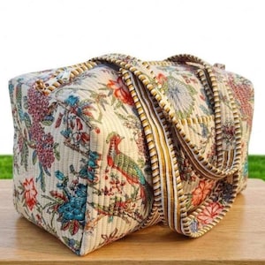 May include: A quilted travel bag with a floral and bird pattern in shades of red, blue, and green on an off-white background. The bag has a rectangular shape with a top handle and a side pocket. The bag is sitting on a wooden surface.