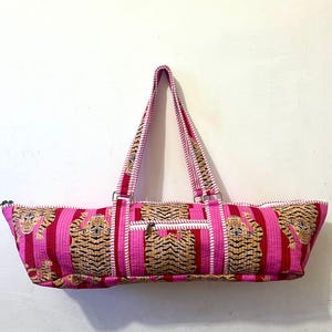 May include: A pink and red striped tote bag with a tiger print design. The bag has a zipper closure, a small front pocket, and two handles. The handles and the front pocket have a tiger print design.
