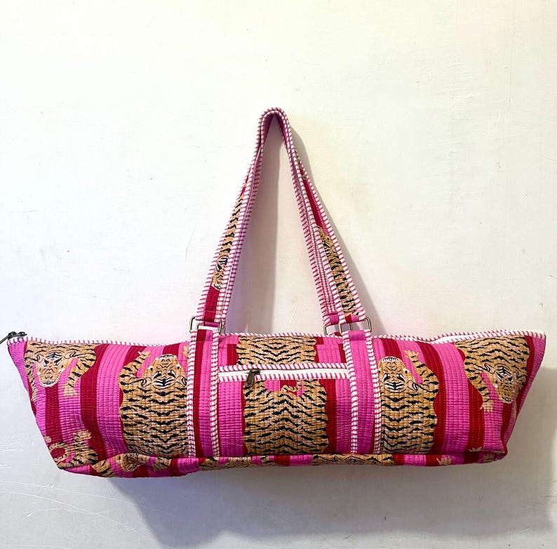 May include: A pink and red striped tote bag with a tiger print design. The bag has a zipper closure, a small front pocket, and two handles. The handles and the front pocket have a tiger print design.