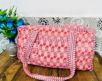 May include: A pink and white floral patterned cotton duffel bag with black and white striped straps.