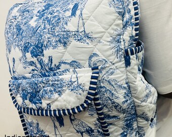 Peut inclure: Sac à dos matelassé blanc et bleu avec un motif de toile de Jouy représentant des oiseaux et des feuillages. Le sac à dos a une poche à rabat et est bordé d'un passepoil rayé bleu et blanc. Les bretelles et la poignée sont blanches.