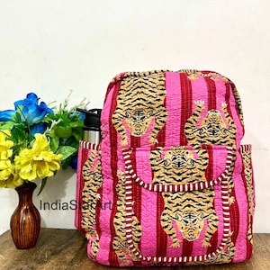 May include: A quilted backpack with a pink and red striped pattern, featuring tiger face designs. The backpack has a front pocket and side pockets. A water bottle is in the side pocket. The text "IndiaStart" is visible.