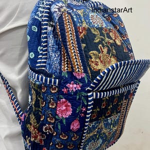 May include: A patchwork backpack with a variety of blue floral and patterned fabrics. The backpack has a front pocket with white and blue stripes and adjustable straps. The design includes floral and paisley patterns in shades of blue, brown, and pink.