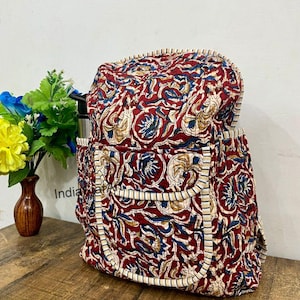 May include: A quilted backpack with a vibrant floral pattern in shades of red, blue, and beige. The backpack has a rectangular shape with a top flap and two side pockets. The edges are trimmed with a white and black striped fabric.