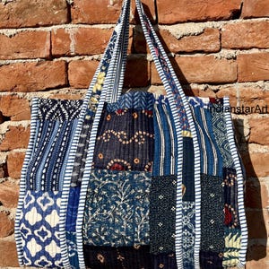 Puede incluir: Un gran bolso tote azul y blanco de patchwork con un diseño acolchado. El bolso tiene una base ancha y dos asas largas. El bolso está hecho de diferentes telas con varios patrones, incluyendo rayas, diseños florales y formas geométricas.