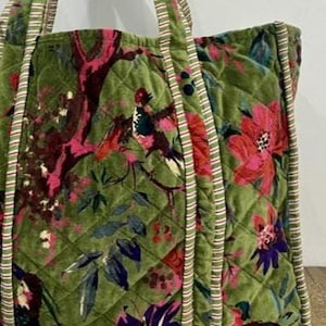 May include: Green quilted tote bag with a floral and bird pattern in shades of pink, red, and purple. The bag has striped handles and trim. The bag is made of a soft, velvety material.